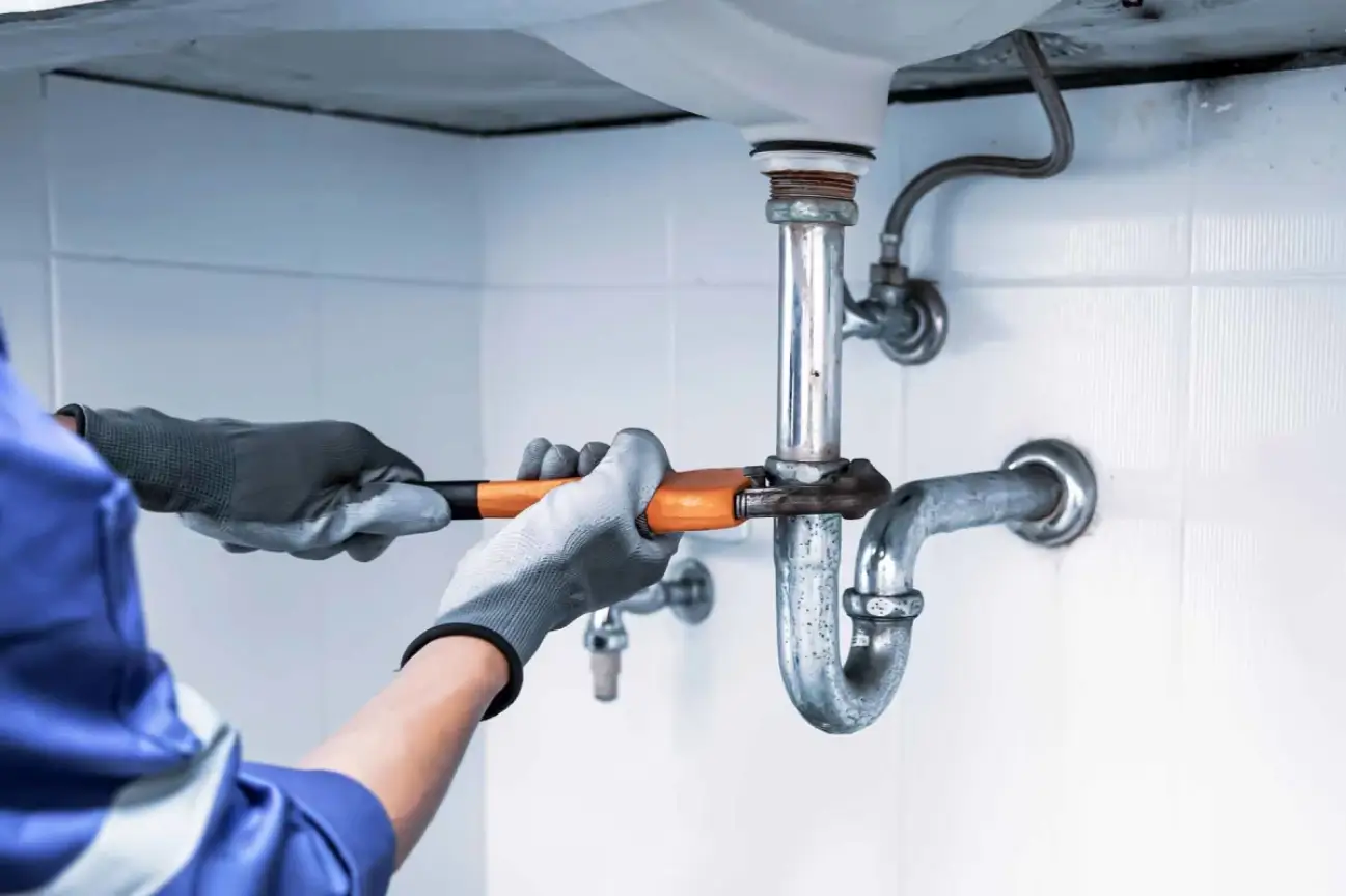 Friendly Build & Fix plumbing use a wrench to service under-sink pipes in a tiled bathroom