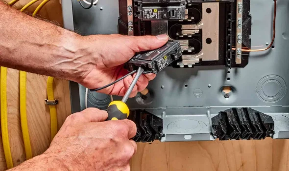 Friendly Build & Fix technician performing electrical panel maintenance with screwdriver and circuit breaker