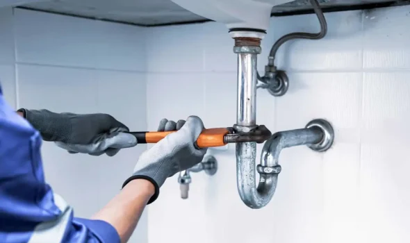 Friendly Build & Fix technician tightening a P-trap pipe beneath a sink during plumbing repair