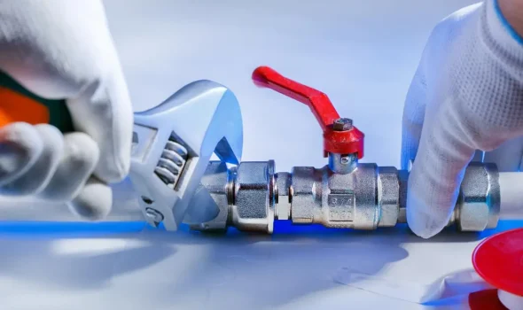 Close-up of Friendly Build & Fix plumber adjusting metal valve with wrench during plumbing service